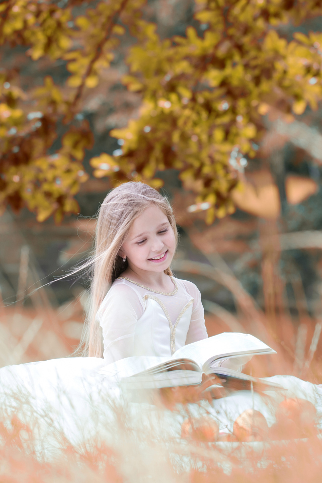 Девочка в красивом белом платье читает книгу на природе