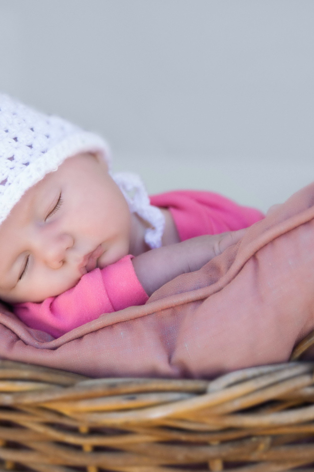 Маленький ребенок в белой шапке спит в корзине