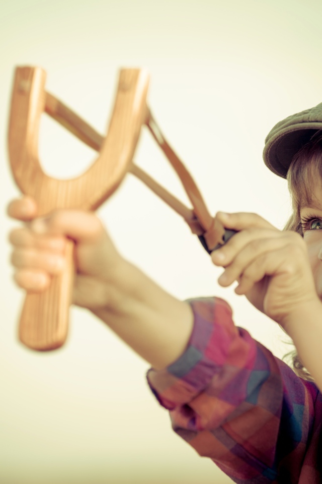 Маленький мальчик в кепке целится с рогатки