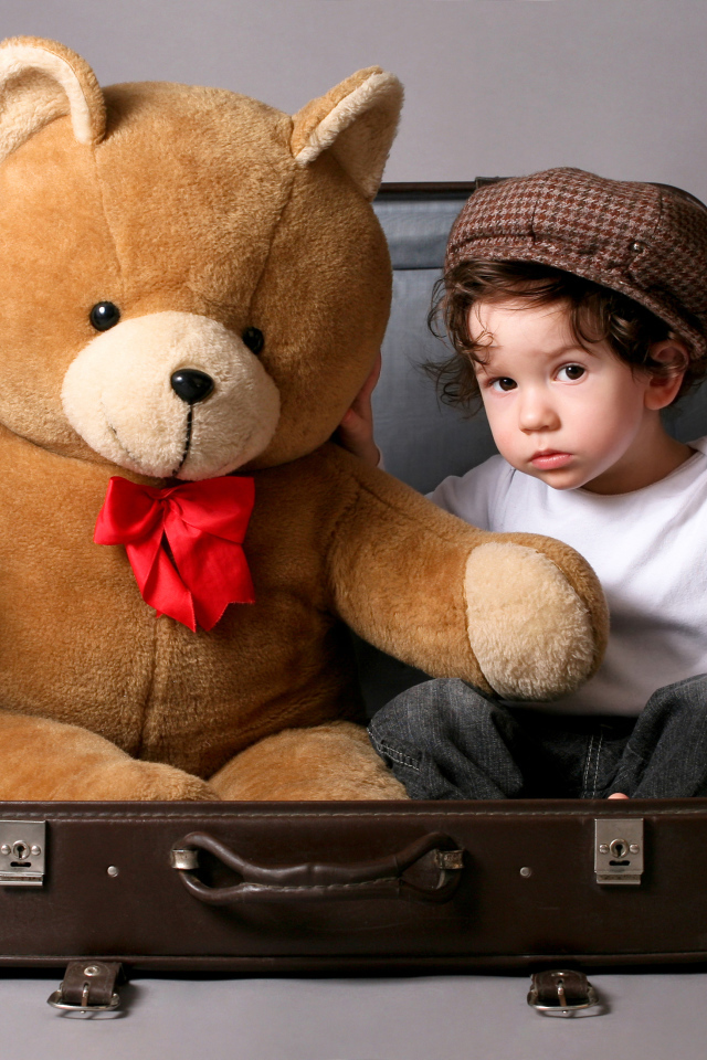 Маленький мальчик сидит в чемодане с плюшевым мишкой 