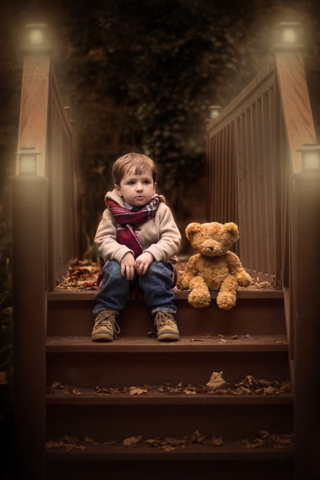 Маленький мальчик сидит с игрушечным мишкой на ступеньках