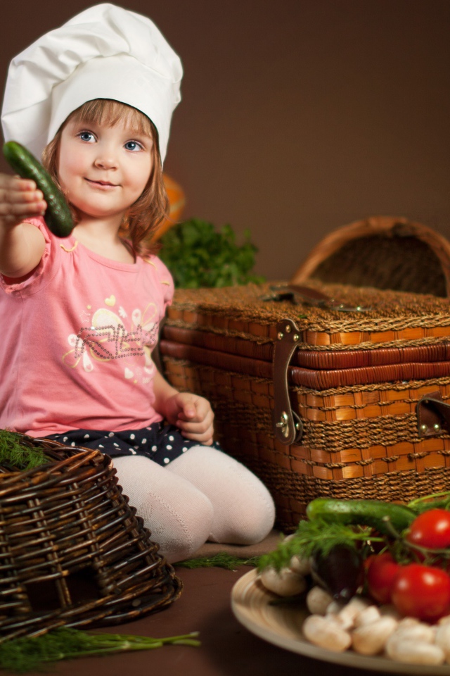 Маленькая девочка в шапке повара с огурцом в руках