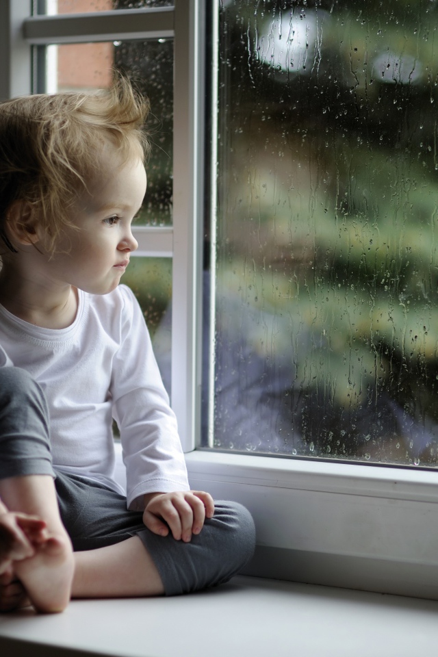 Маленькая девочка сидит на подоконнике у окна