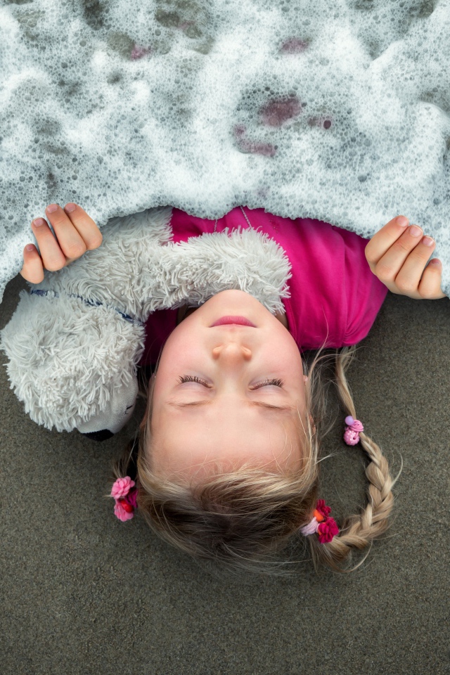 Маленькая девочка спит на песке под одеялом из морской пены