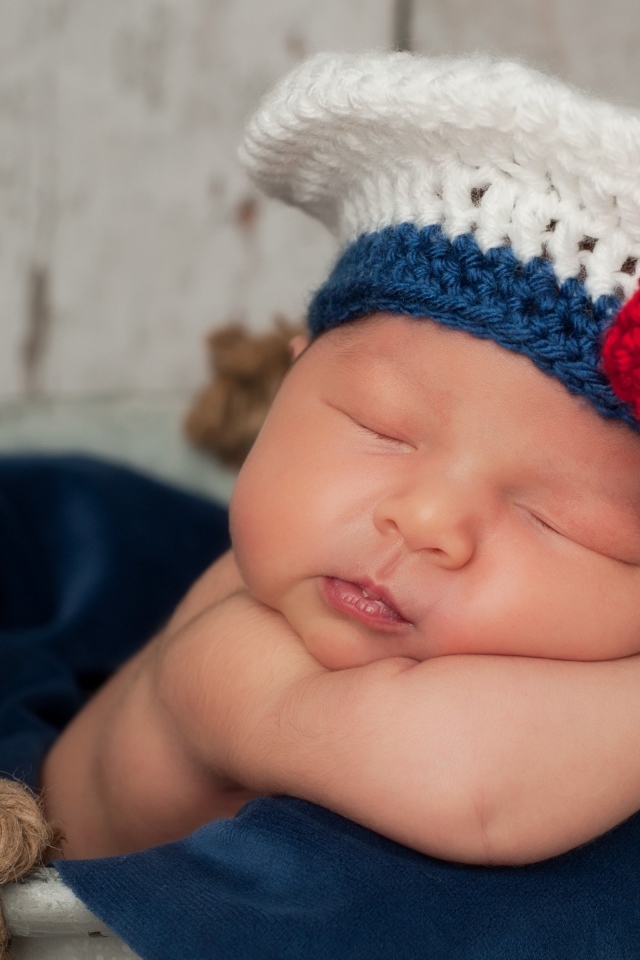 Спящий грудной ребенок в вязаной шапочке с красным бантом
