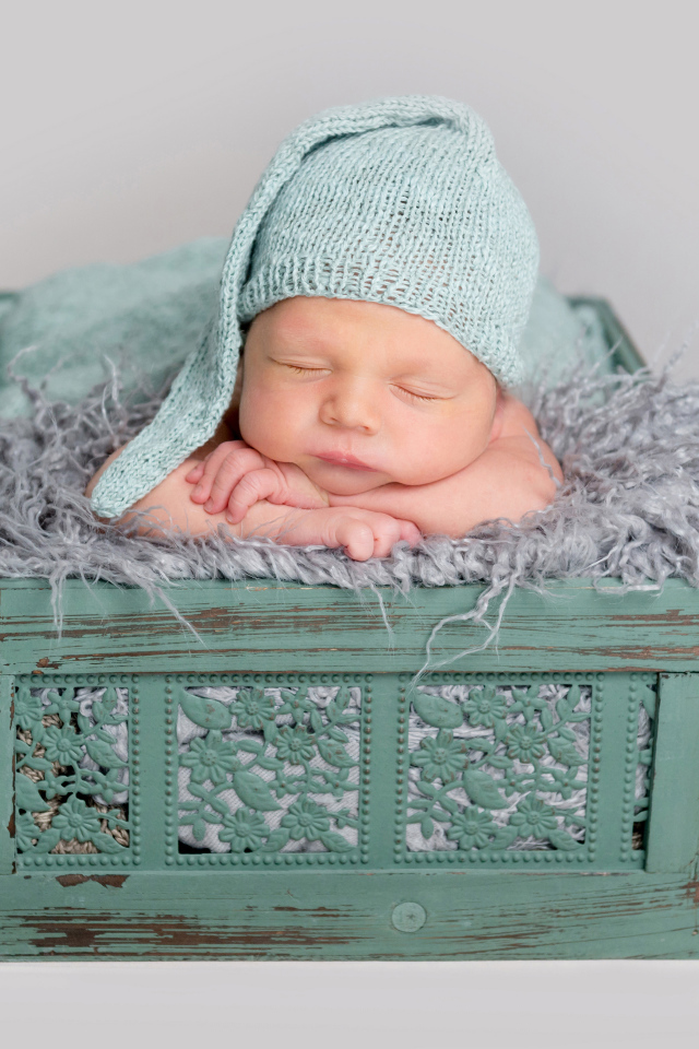 Спящий ребенок в зеленом ящике на сером фоне