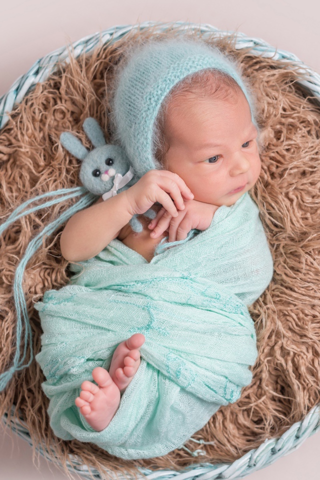 Маленький ребенок в корзине на сером фоне