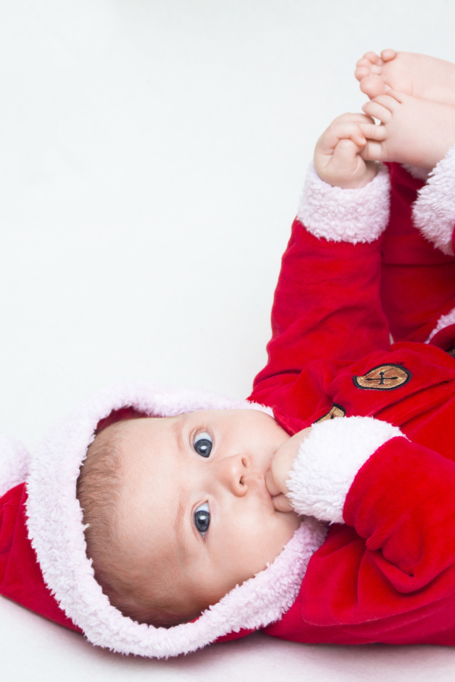 Маленький ребенок в красном новогоднем костюме на сером фоне