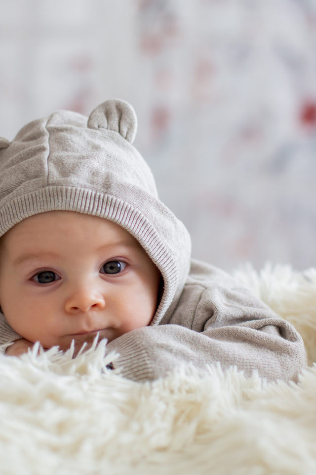 Маленький ребенок лежит на белом меховом покрывале 