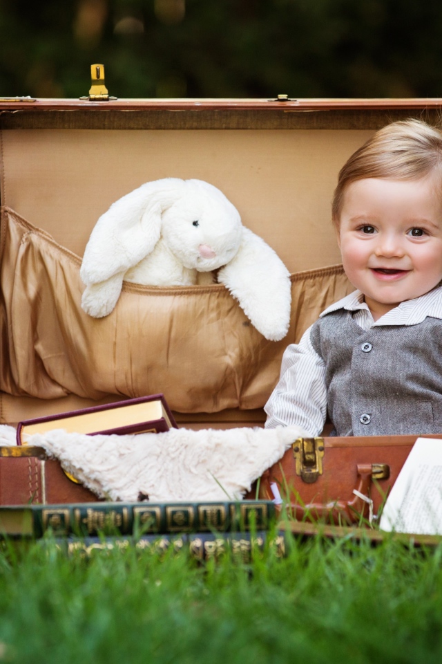 Улыбающийся мальчик сидит в чемодане с книгами