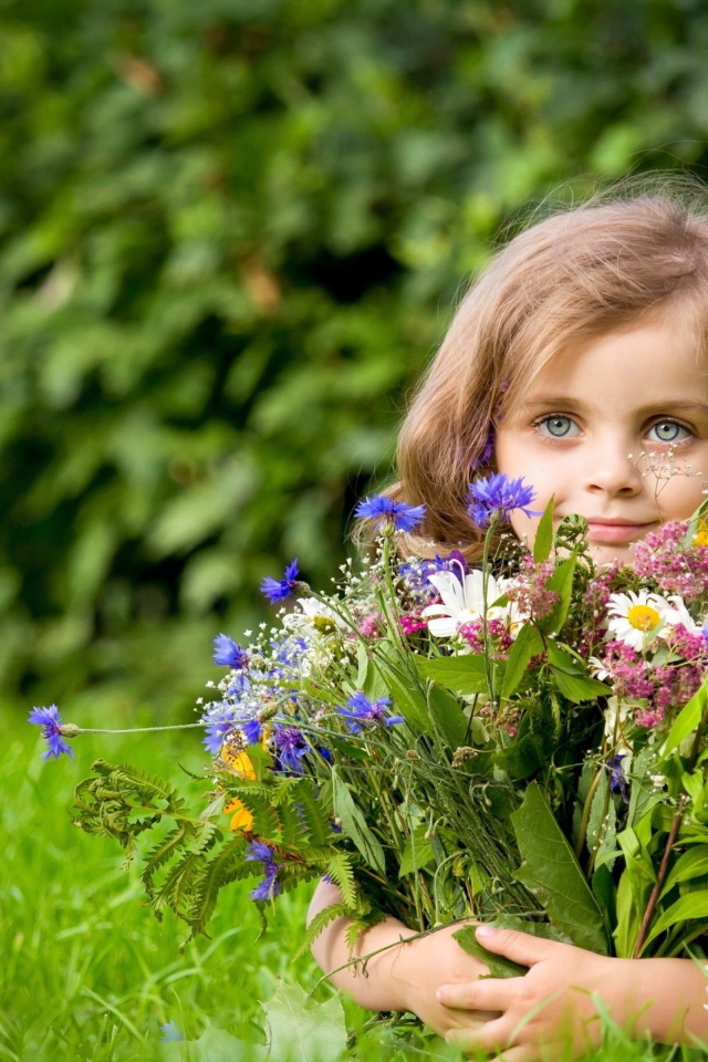 Красивая девочка с букетом цветов лежит на зеленой траве