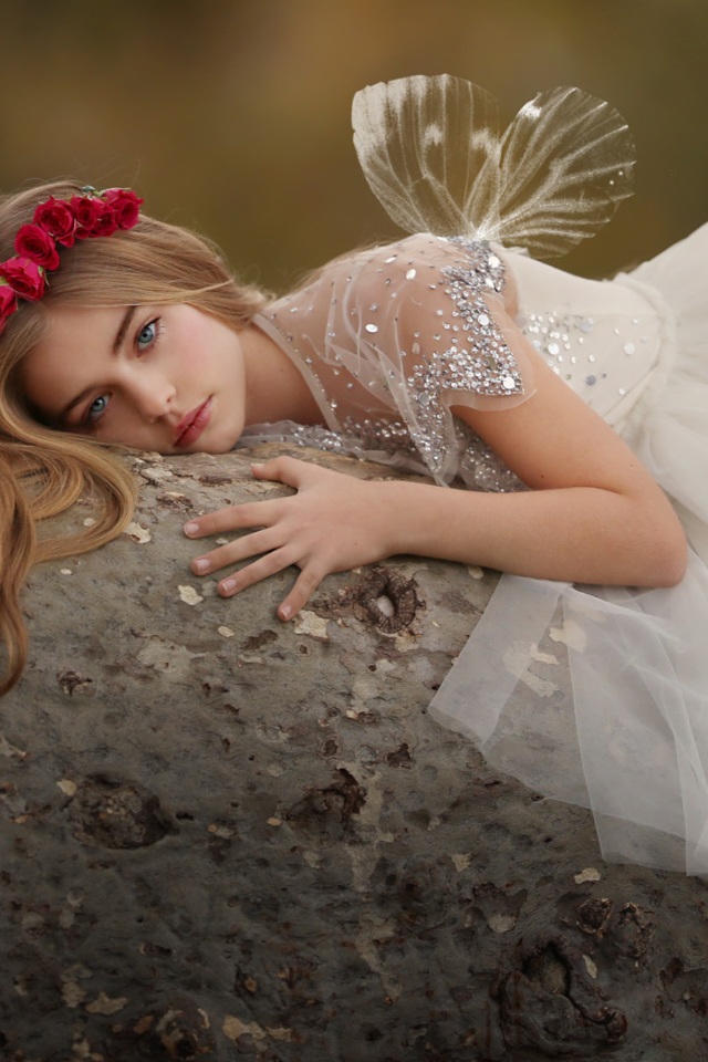 Красивая маленькая девочка в белом платье лежит на камне