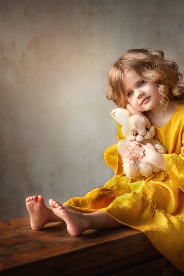 Beautiful little girl in yellow dress with toy