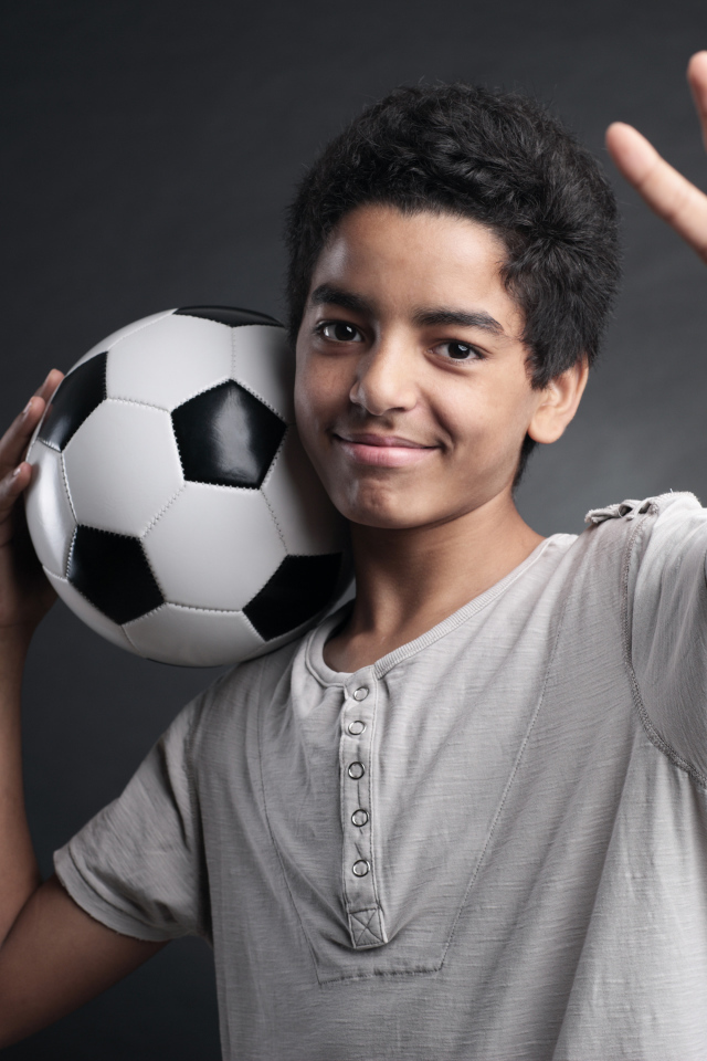 Мальчик с футбольным мячом на плече на сером фоне