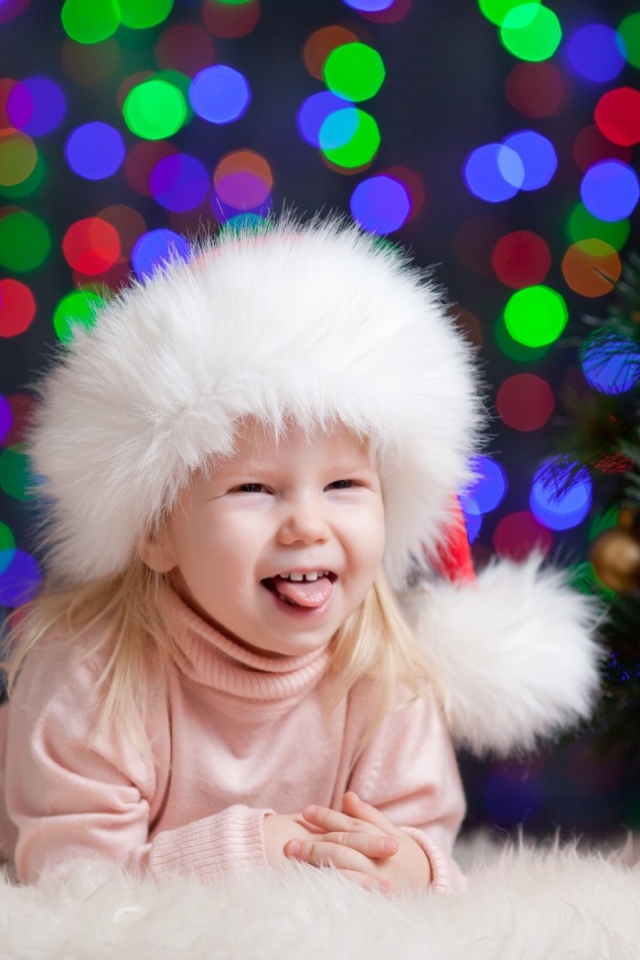 Смешная девочка в новогодней шапке у елки