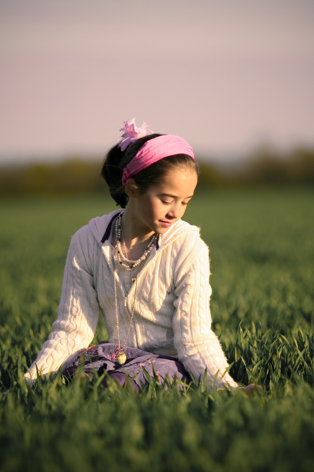 Девочка с розовой повязкой на голове сидит в зеленой траве