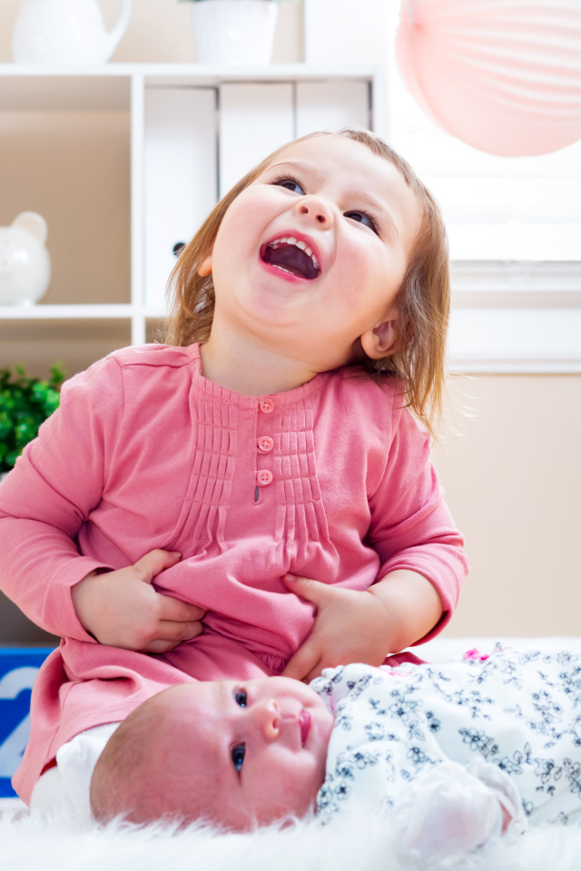 Смеющаяся маленькая девочка с младенцем