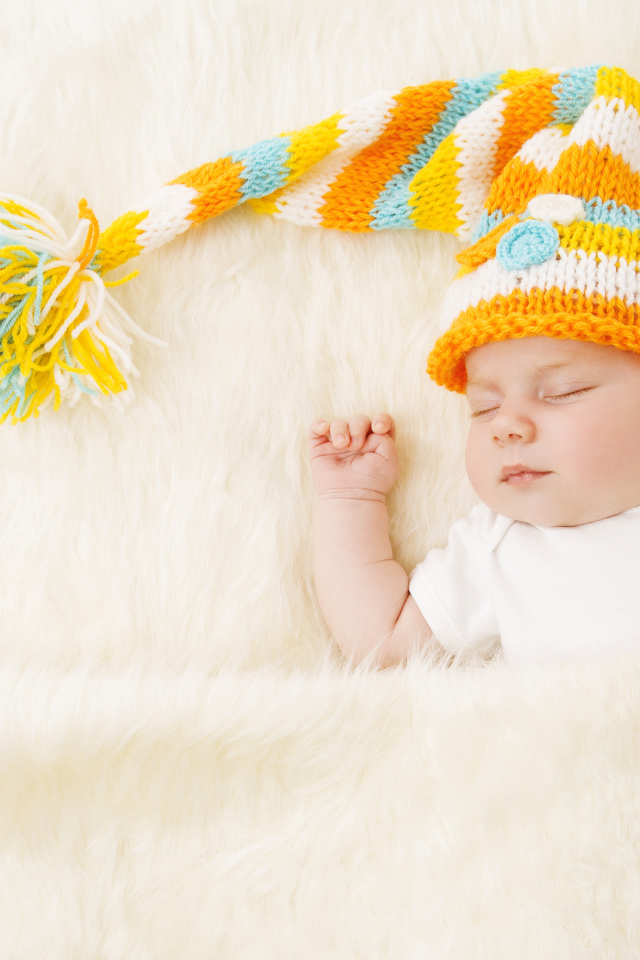 Маленький спящий под меховым покрывалом малыш в вязаной шапке