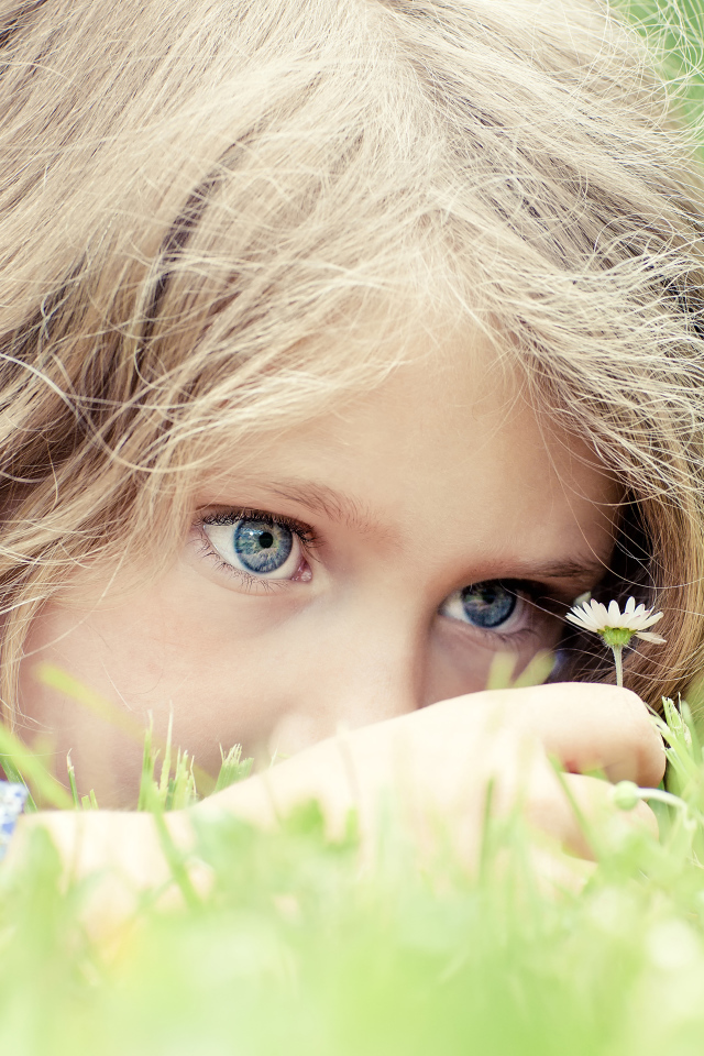 Маленькая голубоглазая девочка на траве с ромашкой