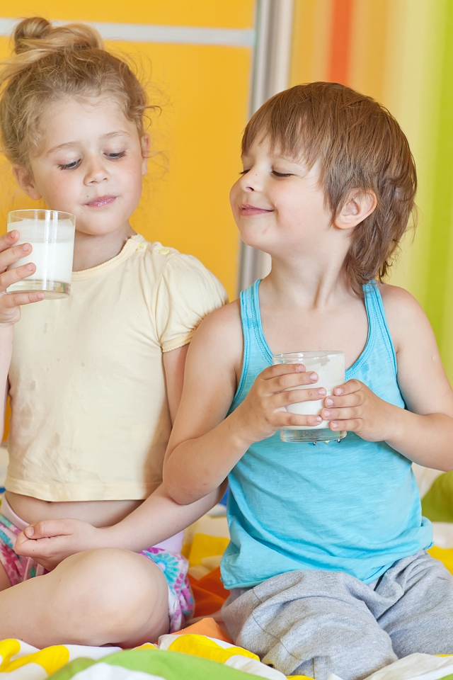 Маленькие мальчик и девочка со стаканами молока в руках 