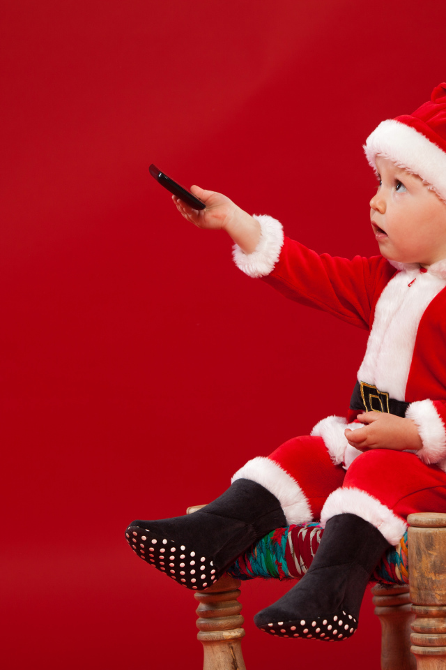 Маленький мальчик в костюме Санта Клауса сидит на стуле на красном фоне