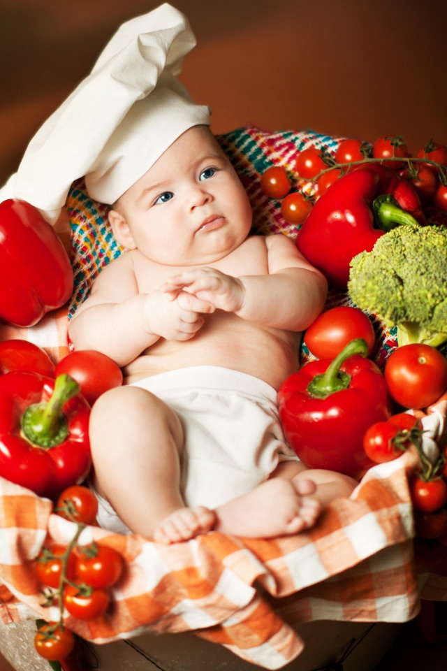 Маленький мальчик в костюме повара в корзине с перцем и помидорами