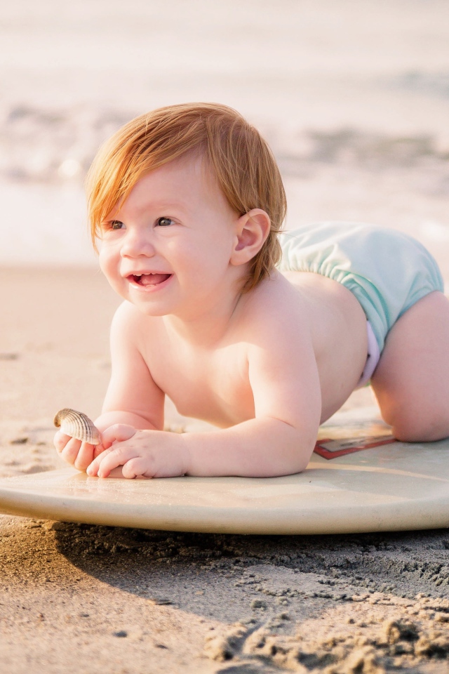 Маленький мальчик на доске для серфинга на пляже