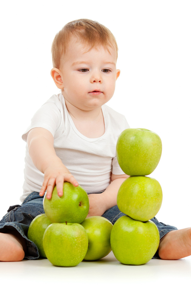 Маленький мальчик играет с зелеными яблоками на белом фоне