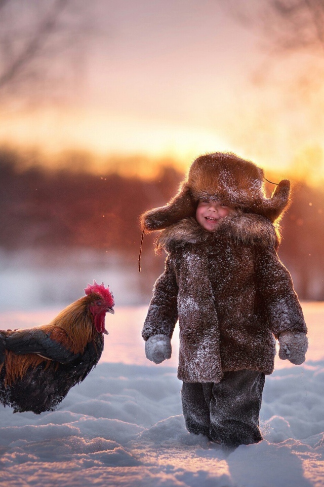 Маленький мальчик с петухом на снегу зимой