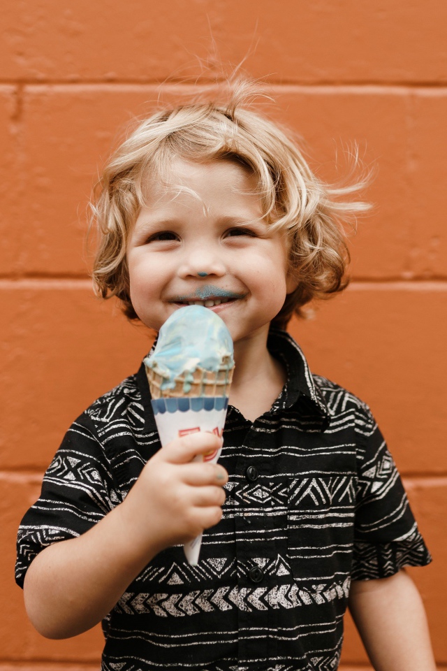 Маленький мальчик с мороженым в руках у стены