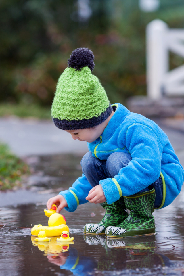Маленький мальчик с резиновыми уточками в луже осенью