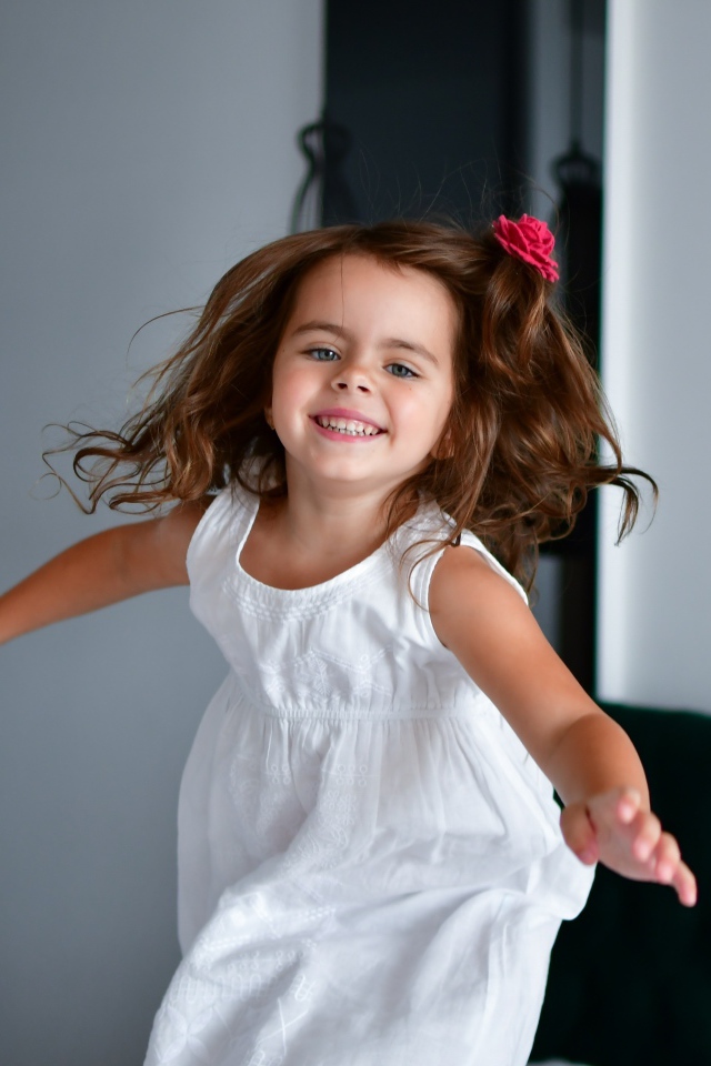 Маленькая веселая девочка в белом платье