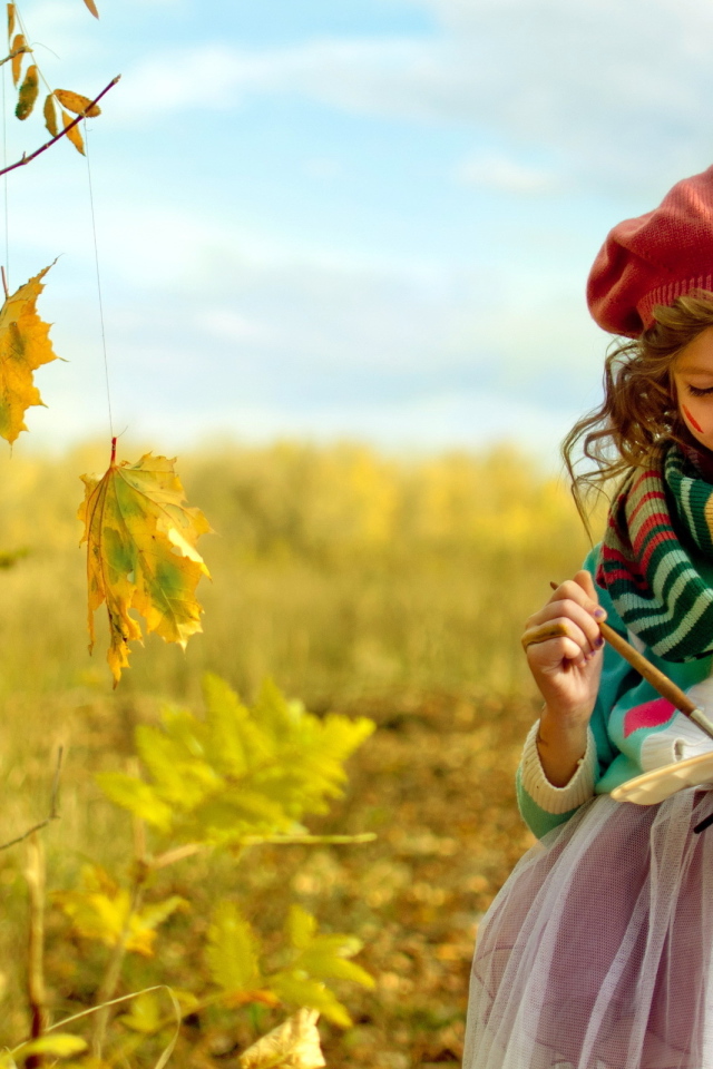 Маленькая девочка рисует красками на листьях осенью 