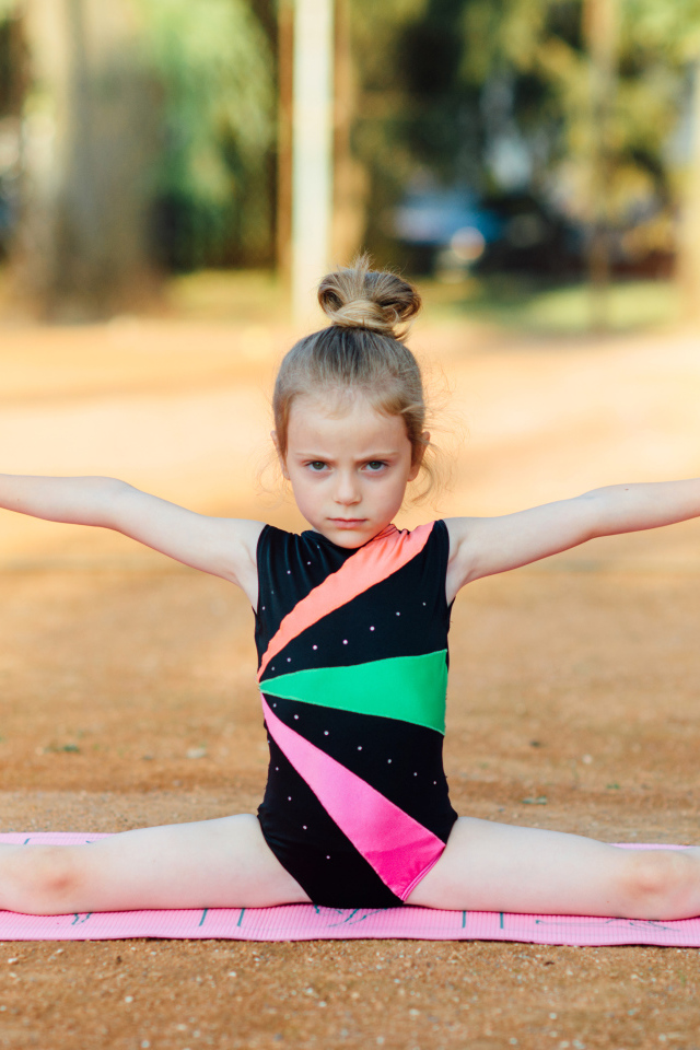Маленькая девочка гимнастка сидит на шпагате 