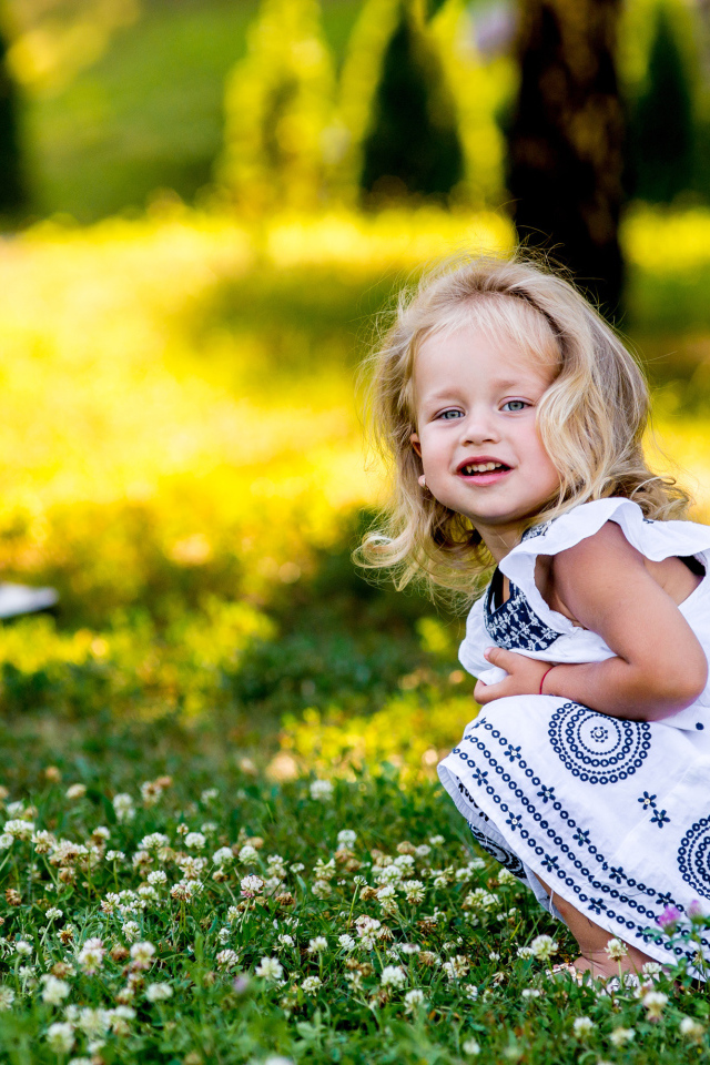 Маленькая девочка в красивом платье сидит на зеленой траве