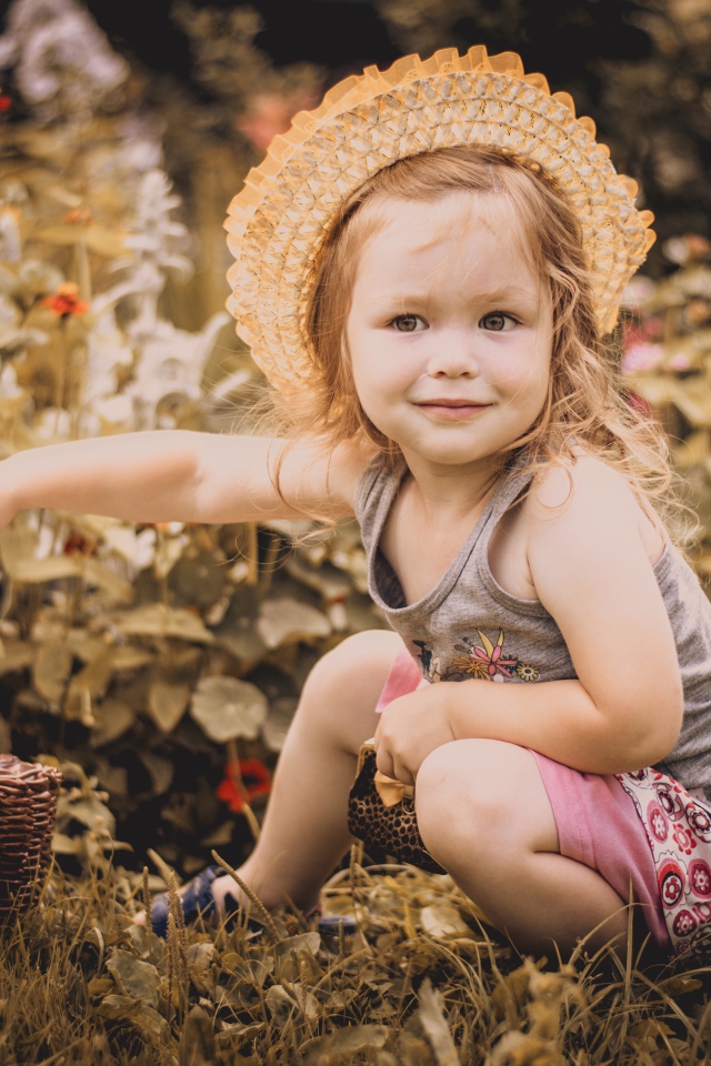 Маленькая девочка в шляпе сидит на траве с корзиной