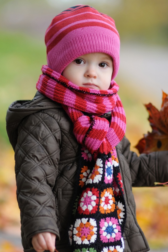Маленькая девочка в розовой шапке с листьями в руке