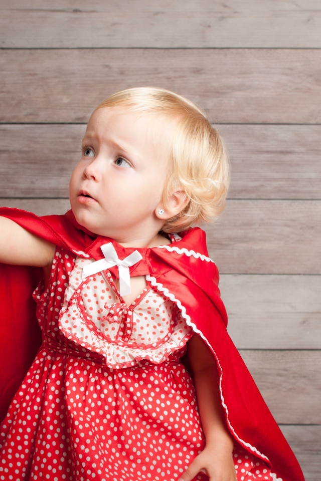 Маленькая девочка в красном платье ловит мыльный пузырь