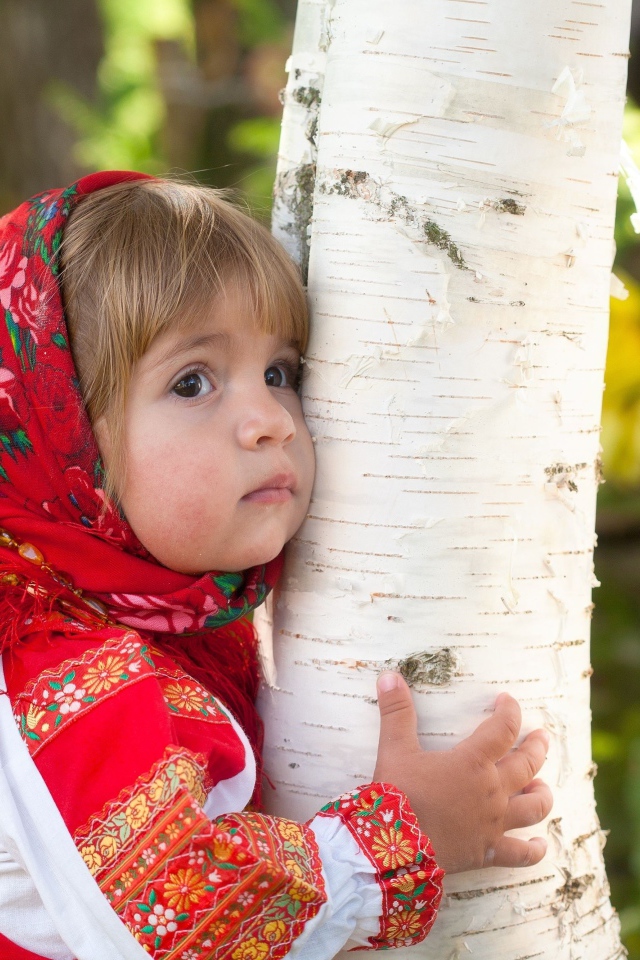 Маленькая девочка в красном платке обнимает березу