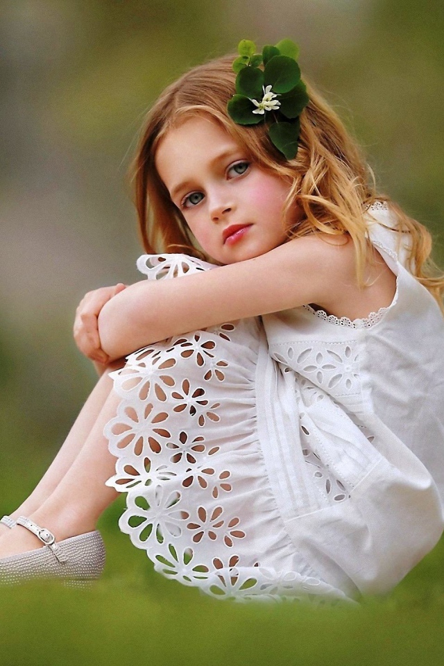 Маленькая девочка в белом платье сидит на зеленой траве