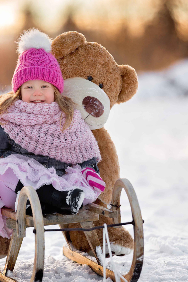 Маленькая девочка на санках с большим медведем зимой 