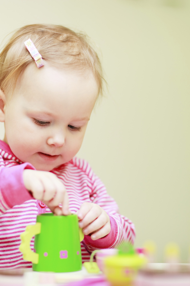 Маленькая девочка играет с посудой 