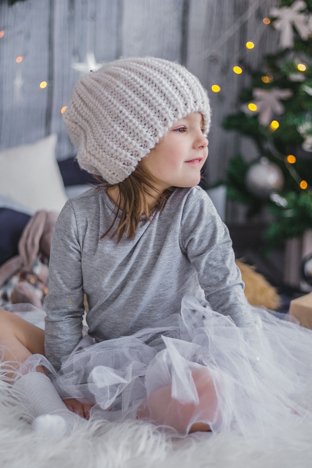 Маленькая девочка сидит на кровати у новогодней елки