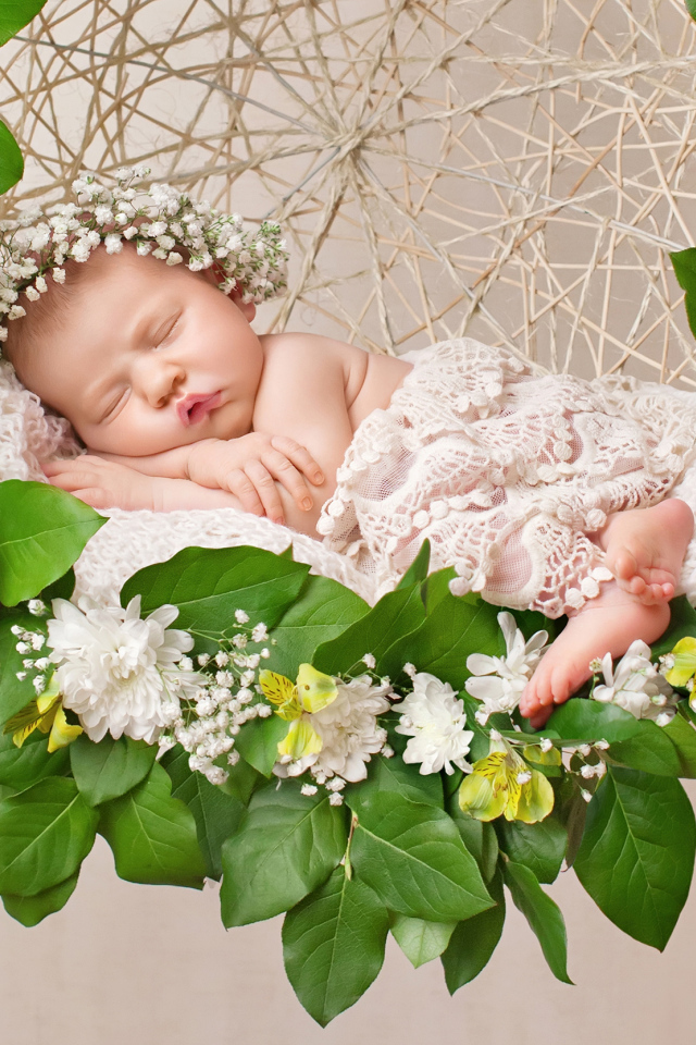 Маленькая девочка спит в колыбеле украшенной зелеными листьями