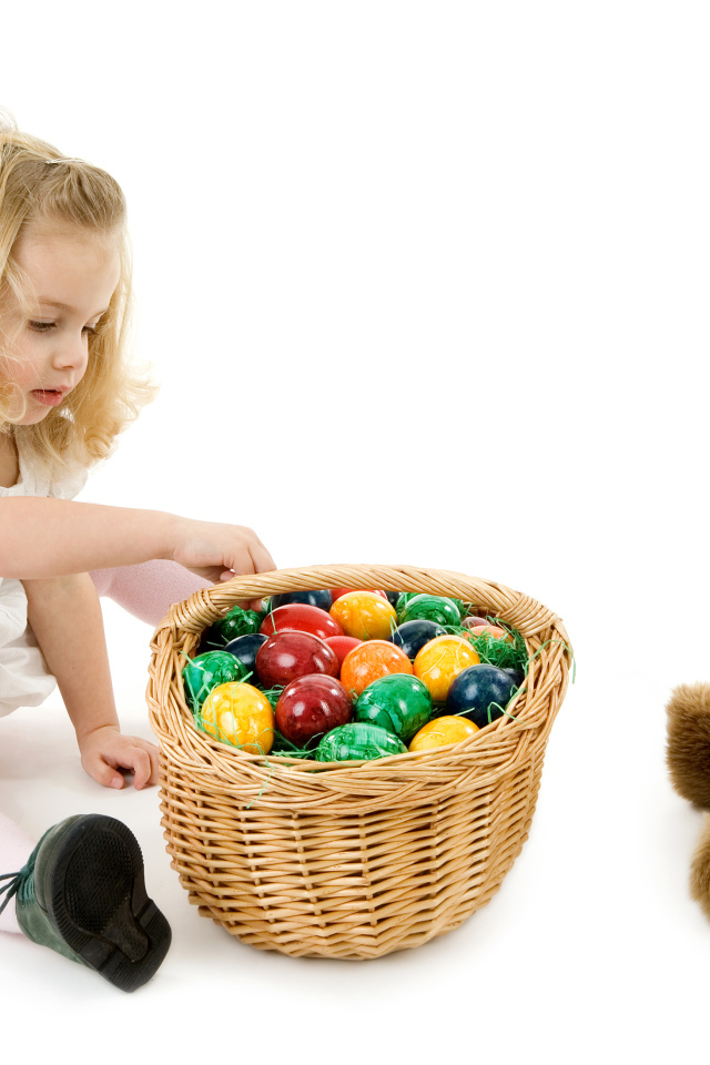 Маленькая девочка с корзиной пасхальных яиц и игрушкой на белом фоне