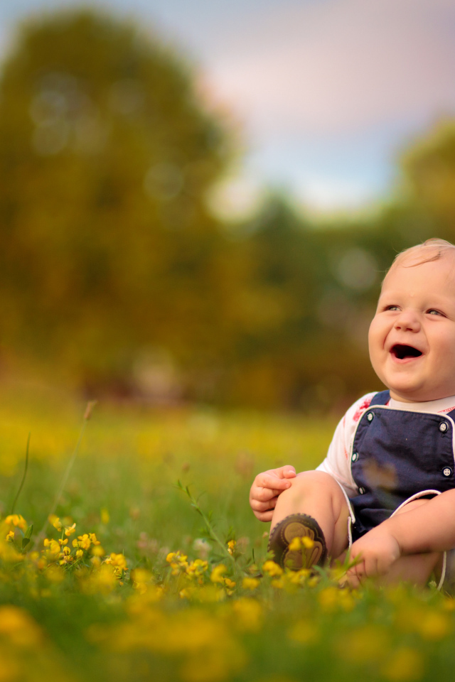 Маленький смеющийся мальчик сидит на траве с желтыми цветами