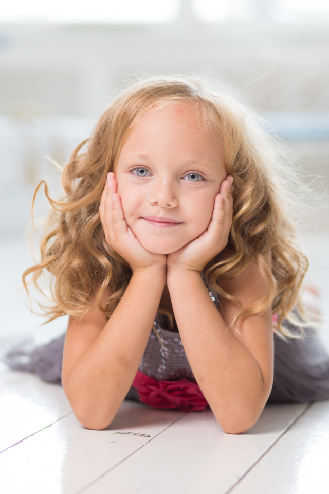 Маленькая длинноволосая голубоглазая девочка лежит на полу
