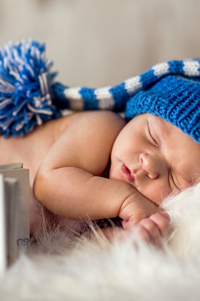 Маленький спящий грудной ребенок в синей вязанной шапке 