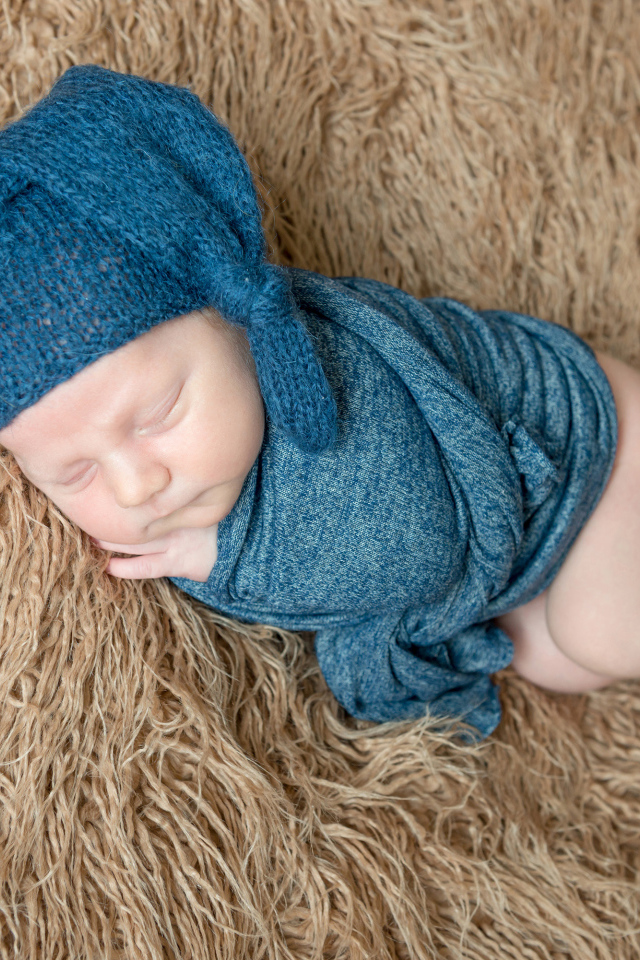 Маленький спящий грудной ребенок в синей вязаной шапке на меховом покрывале 