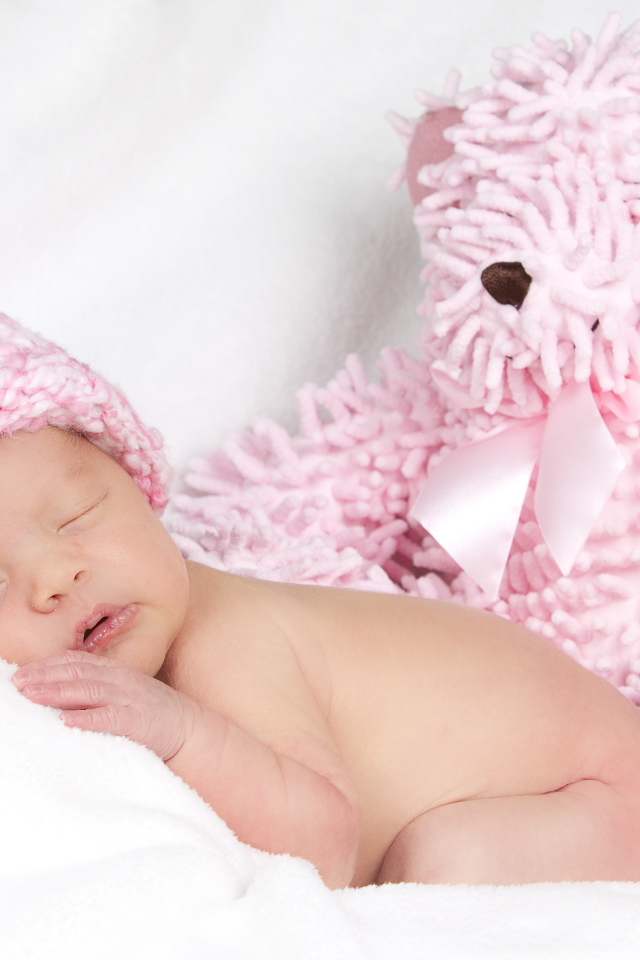 Маленький спящий ребенок в розовой шапке с игрушечным мишкой